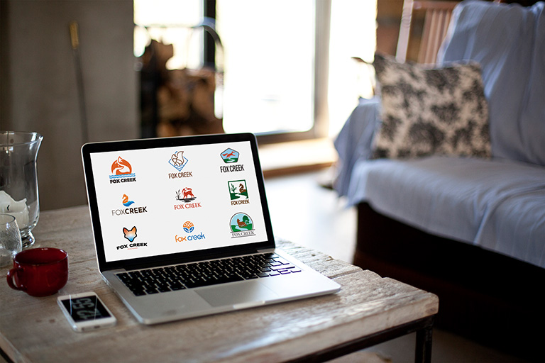 Macbook sitting on a table. 9 examples of logos are displayed on the screen.