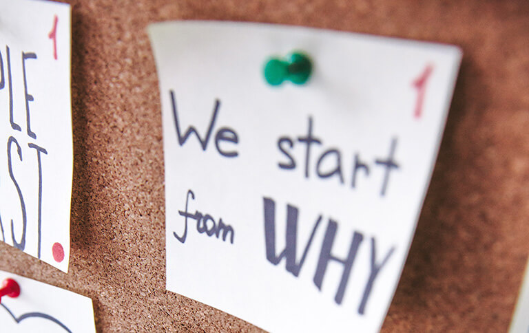 White post it note reading "We start from WHY" pinned to cork board.
