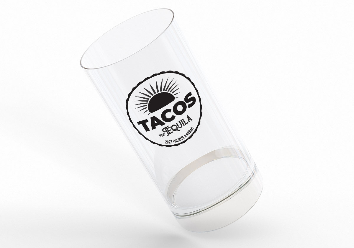 Clear shot glass at angle with black Tacos & tequila logo.